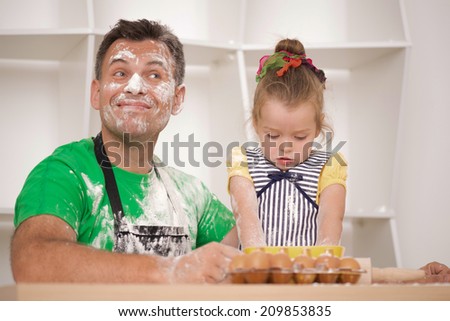 Half-length portrait of cute little daughter with happy handsome father cooking pastry, mixing flour and having fun, low angle