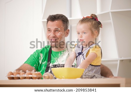 Half-length portrait of cute little daughter with happy handsome father cooking pastry, mixing flour and having fun. Father showing a rolling pin