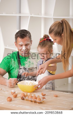Family portrait, cute little daughter with handsome father and beautiful mother cooking pastry, mom showing how to knead dough, top view
