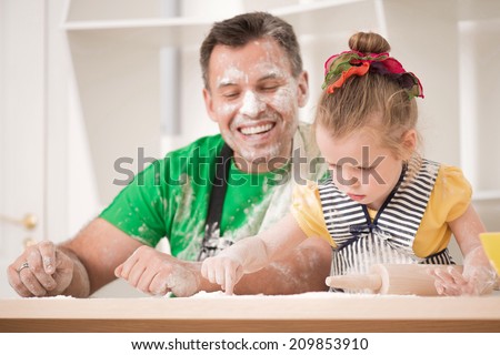 Half-length portrait of cute little daughter with handsome father cooking pastry, working with rolling pin. Dirty aprons