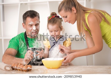 Family portrait, cute little daughter with handsome father and beautiful mother cooking pastry, mom showing how to mix flour