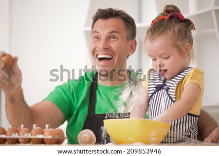 Half-length portrait of cute little daughter with happy handsome father cooking pastry, mixing flour and having fun. Kid throwing flour at father