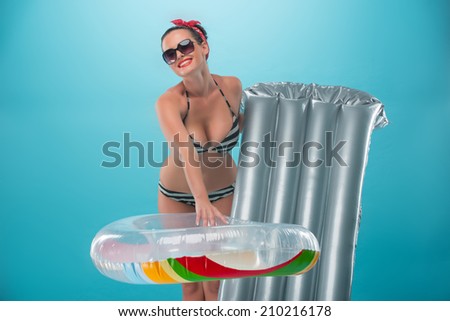 Beautiful seductive girl with pretty smile in pinup style in swimsuit holding inflatable ring and mattress, Half-length portrait isolated on blue