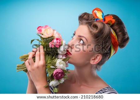 Closeup portrait of beautiful sexy girl with pretty smile in pinup style wearing navy color dress posing with bouquet of flowers looking up isolated on blue