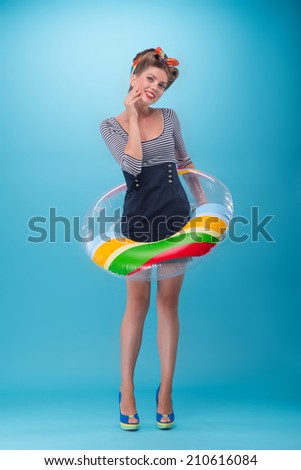 Full length portrait of Beautiful girl with pretty smile in pinup style wearing navy color dress posing with inflatable ring isolated on blue