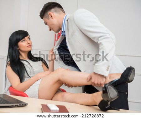 Side view portrait of young business couple in passion looking to each other while woman sitting on the chair at the desk holding the jacket of her colleague and man holding her leg with passion