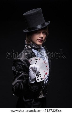Half-length portrait of fair-haired matchless juggler wearing interesting black costume white shirt and topper showing us the pack of cards in his hand. Isolated on black background