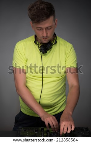 DJ playing music. Confident young DJ with stylish haircut and headphones at work spinning on mixer looking down while standing isolated on dark background