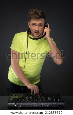 DJ playing music. Confident young DJ with stylish haircut and headphones at work spinning on mixer looking at camera while standing isolated on dark background