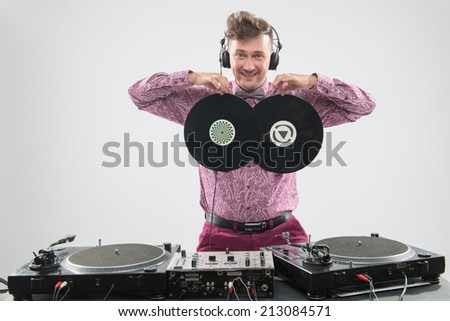 Half-length portrait of excited young DJ with stylish haircut, bow tie and headphones having fun, posing with two vinyl records as boobs by turntable isolated on white background