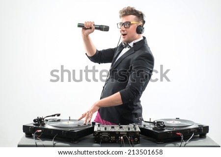 Half-length portrait of stylish emotional DJ in tuxedo spinning and dancing by the turntable with microphone isolated on white background, side view