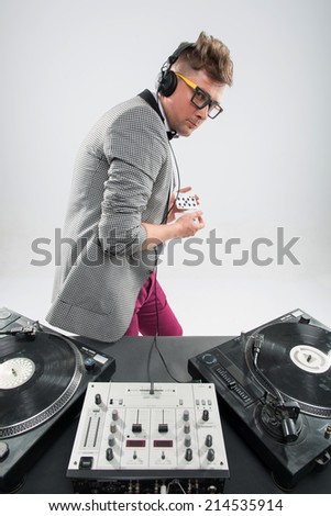 Top view of confident young DJ with stylish haircut and glasses and headphones on head mixing music on mixer and plying with cards standing isolated on white background