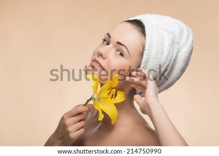 Portrait of girl with clean and  fresh skin with a towel on her head in spa, holding in her hands yellow flower, isolated on beige background