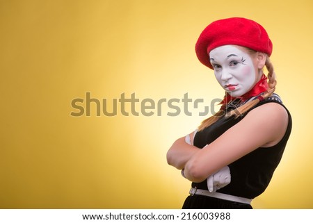 Close-up portrait of indignant female mime with white funny face, red hat and red scarf looking at the camera isolated on yellow background with copy place