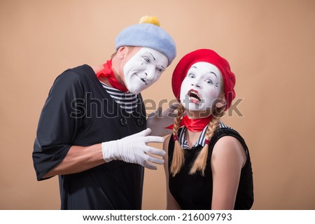 Close-up horizontal portrait of couple of two funny mimes, male mime wanting to touch and to hug a little scared female mime isolated on beige background with copy place