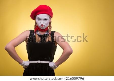 Close-up portrait of indignant female mime with white funny face, red hat and red scarf looking at the camera isolated on yellow background with copy place