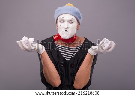 Waist-up portrait of crazy male mime with grey hat and white face holding crumped paper in his hands and looking aside isolated on grey background with copy place