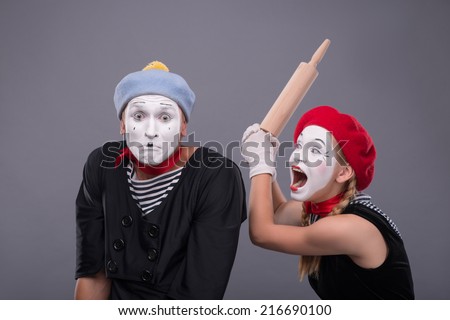 Waist-up portrait of mime couple with white faces, female mime wanting to beat confused male mime with rolling pin isolated on grey background with copy place