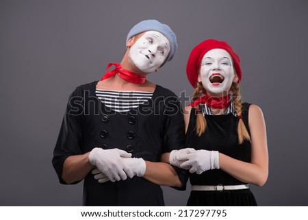 Waist-up portrait of mime couple with white faces, male mime looking at his partner, female mime happy smiling and looking at the camera isolated on grey background with copy place