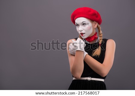 Waist-up portrait of young mime girl looking seductively aside and gently holding her hands on her chest isolated on grey background with copy place