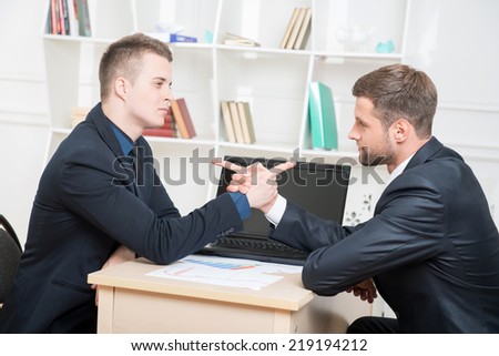 Waist-up portrait of two angry businessmen in suits sitting at the table and armwrestling in office looking on each other with spite thinking about some problems