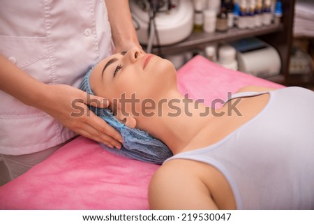 Side-view portrait of a young woman with fresh and clean skin lying on a table getting a light facial massage in healthy beauty spa salon and calmly looking up