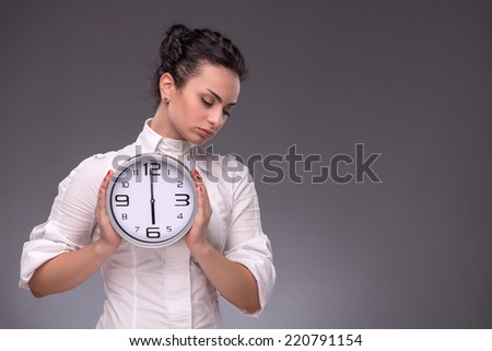 Waist-up portrait of sad girl because she has no time upset holding a big clock in her hands and looking down, isolated on grey background with copy place concept of time management