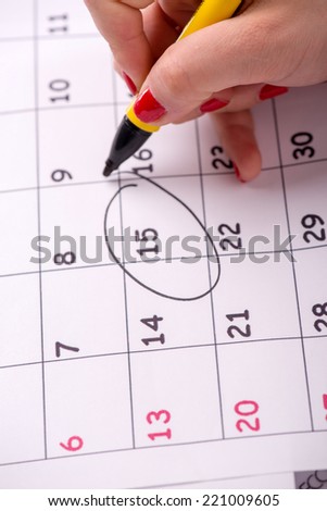 Close-up top-view photo of calendar with a datum circled by young woman with red nails with a back marker, concept of time management at work