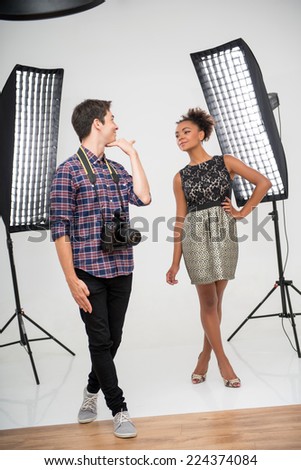 Full- length portrait of young handsome photographer wearing checked shirt standing before the projectors teaching young African model how to pose