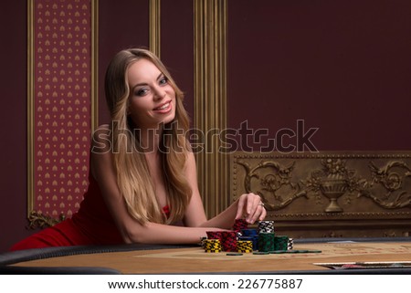 beautiful woman looking at camera  in casino sitting at table with  white blue and red chips  in piles waist up