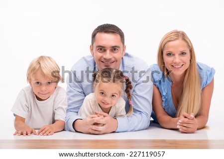 Happy family of father mother son and daughter smiling  lying on stomachs  looking  at camera  isolated on white background