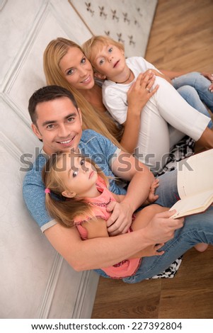 Happy family of father mother son and daughter smiling  looking  at camera sitting reading book   isolated on white background with copy place top view