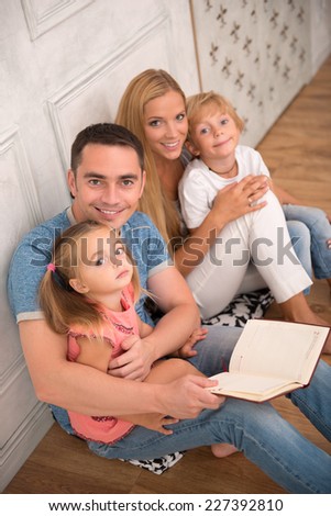 Happy family of father mother son and daughter smiling  looking  at camera sitting reading book   isolated on white background with copy place top view