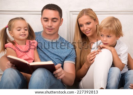 Happy family of father mother son and daughter smiling  looking  at camera sitting reading book   isolated on white background with copy place