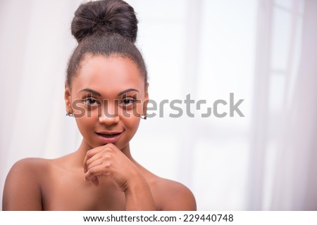 Portrait of beautiful  dark skinned girl in white towel with black curly hair in bun thinking  and touching chin looking at camera isolated on white background  with copy place