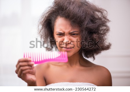 Beautiful  sad disappointed dark skinned girl being not able to  comb her hair looking at rose comb  pulling her face with tangled disorder hair isolated on white background selective focus
