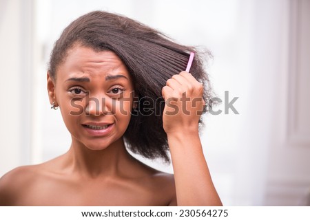 Beautiful  sad disappointed dark skinned girl being not able to  comb her hair looking at camera making efforts pulling her face isolated on white background