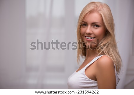Portrait of beautiful  happy blond girl with green  eyes  and straight  hair in white  T shirt  looking at camera   smiling   with copy place