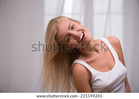 Portrait of beautiful happy blond girl with green  eyes  and straight  hair in white  T shirt  looking at camera smiling opening her mouth