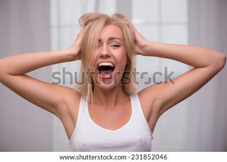 Portrait of beautiful  blond girl in white  T shirt  looking at camera smiling opening mouth tousling her hair crying holding head with hands
