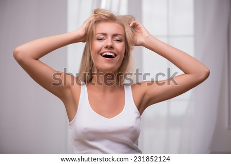 Portrait of beautiful blond girl in white  T shirt  looking at camera smiling opening mouth tousling her hair smiling  holding head with hands