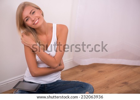 Beautiful happy  blond girl in white  T shirt  and jeans and trainers smiling looking at camera sitting on floor  in lotus pose with copy place waist up