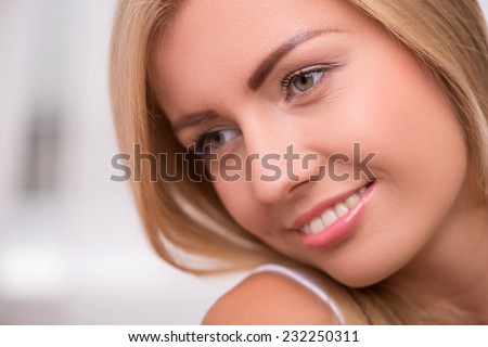 Portrait of beautiful  happy blond girl with green  eyes  and straight  hair in white  T shirt  looking aside smiling    close up