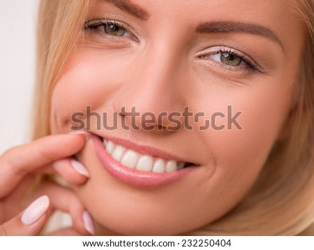 Portrait of beautiful  happy blond girl with green  eyes  and straight  hair in white  T shirt  looking at camera  touching her face  smiling   close up