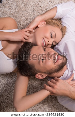 Portrait of happy couple in love of handsome man looking at camera and attractive woman looking at him smiling embracing  lying on carpet