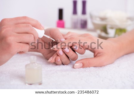 manicurist doing manicure  client  painting nails with transparent nail polish  in salon  on white towel