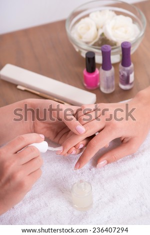 manicurist doing manicure  client  painting nails with transparent nail polish  in salon  on white towel  top view
