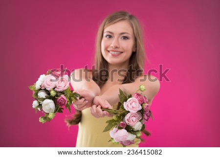 Portrait of happy beautiful brown haired girl holding  bunches  of roses on rose background smiling looking at camera  waist up