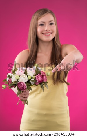 Portrait of happy beautiful brown haired girl putting at   bunch of roses on rose background smiling looking at camera  waist up selective focus