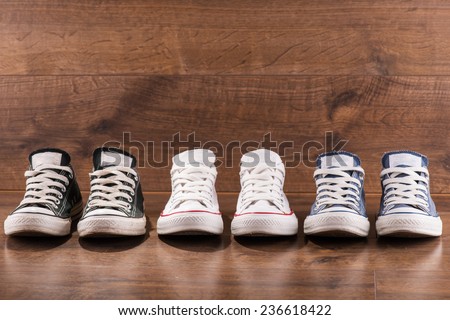 three pairs of cool youth white gym shoes with red  stripes  on brown wooden floor  standing in line with copy place